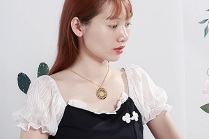 Model wearing gold circular pendant necklace with Roman numeral engravings in high detail