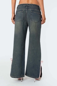 Détail du pantalon en jean évasé avec fentes latérales et nœuds en ruban de soie rose