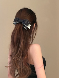 Detailed back view of a navy blue polka dot ribbon bow hair clip on model's hair