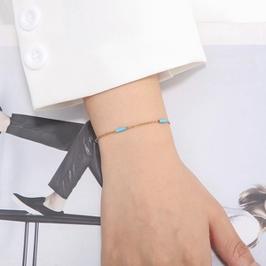 Détail d'un bracelet en chaîne dorée avec des perles cylindriques en émail bleu