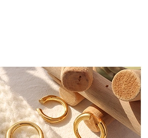 Detailed view of three gold-plated metal ear cuffs on wooden and knit backgrounds