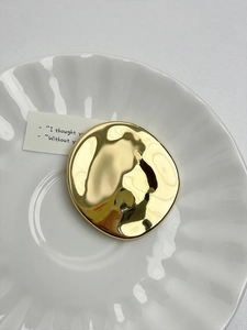 Macro detail of glossy golden irregular oval brooch on a white ceramic dish
