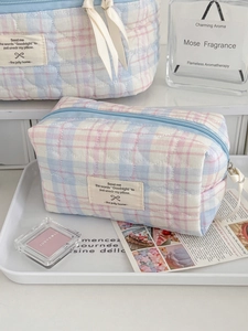 Pastel plaid quilted makeup bag with heart stitching and woven label on a white tray