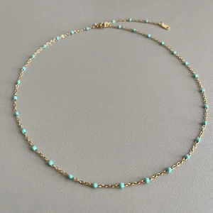 Detail of a thin gold titanium necklace with small green enamel beads on a grey background
