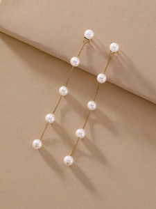 Detail shot of elegant long tassel earrings with faux pearls and silver needles on beige paper