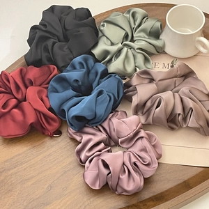 Detailed view of assorted satin hair scrunchies in Morandi colors on a wood tray