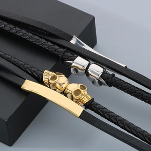 Detail of layered black leather bracelets with gold and silver skull charms on a pedestal