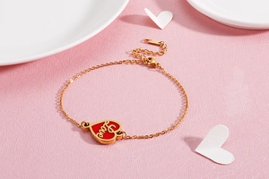 Close-up of gold stainless steel bracelet with red enamel heart pendant and Love engraving