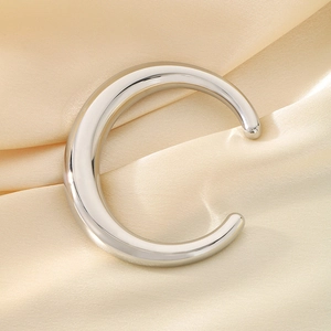 Détail macro d'un bracelet ouvert argenté en C sur un fond de satin champagne élégant