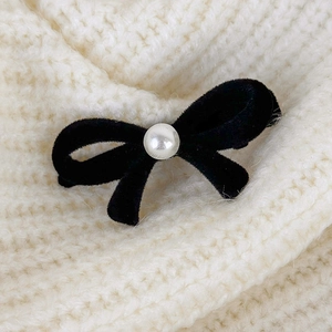 Close-up of black velvet bow hair clip with a pearl center on a soft knit background