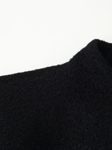 Close-up of black wool blend fabric showing detailed curly lamb wool texture and fiber