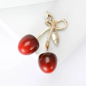 Chic cherry brooch with red resin fruit and golden metal leaves on a minimalist base