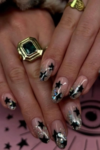 Close-up of nude almond press-on nails with black stars and silver glitter accents