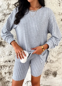 Detail of grey ribbed knit long sleeve top and cycling shorts on a model against a stone wall