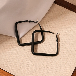 Close-up of large black square geometric earrings on a minimalist cream woven fabric background