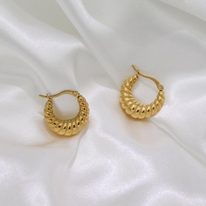 Close-up of gold plated croissant dome hoop earrings on white silk fabric background