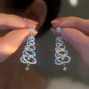 Close-up of sparkling Christmas tree earrings with colorful crystals held by hand