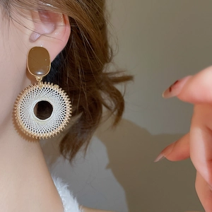 Detail of bohemian woven geometric hoop earrings in brown and beige with golden metal accents