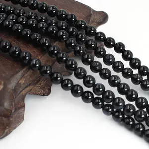 Detail view of polished black agate round beads draped over a dark wooden base