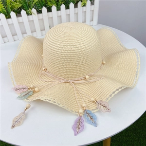 Detailed top view of wide brim straw sun hat with colorful leaf charms on a table