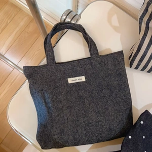 Minimalist dark gray denim tote bag with simple wish label on white podium