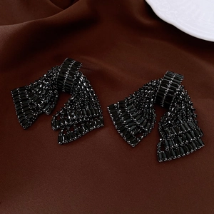 Detail of black crystal bow earrings on silk fabric with elegant rhinestone sparkles