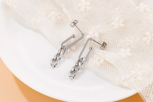 Detail view of silver metal chain earrings on white ceramic plate with lace background