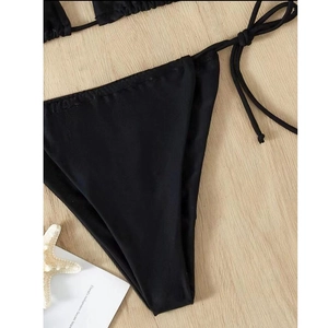 Detail of black side-tie bikini bottom with ribbed texture on wooden background