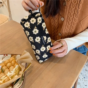 Floral canvas pencil case with black zipper held in a warm lifestyle restaurant setting