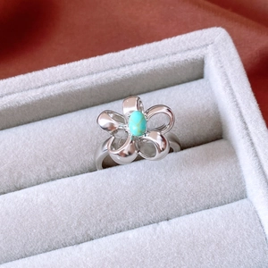 Detailed close-up of a vintage silver flower ring with turquoise stone on grey velvet