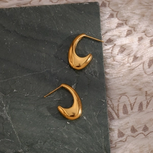 Close-up of polished gold hook earrings on dark stone and white faux fur background