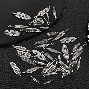 Vintage silver alloy feather pendants in various sizes on black leather surface