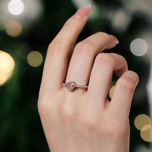 Close-up of heart-shaped silver ring with rose gold bow on model finger