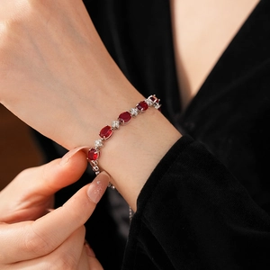 Close-up of elegant ruby red oval stones and flower zircon bracelet on woman's wrist