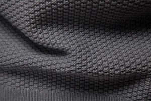 Dettaglio macro del tessuto a maglia grigio scuro con trama a nido d'ape e bordo a coste