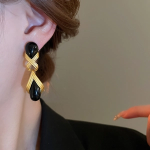 Close-up of vintage resin teardrop earrings with gold metallic cross detail on a model