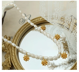 Detail of freshwater pearl necklace with five golden daisy pendants on a vintage mirror