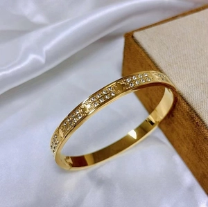 Detailed macro view of gold clover bangle with pavé crystals on white satin background