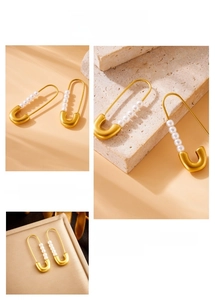 Detail of gold-plated safety pin earrings with five white pearls and matte finish