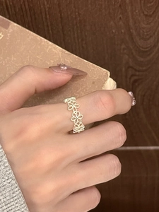 Macro detail of silver floral hollow open ring worn on finger with vintage backdrop