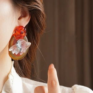 Detail of red rose and amber goldfish floral earring worn on a model's ear