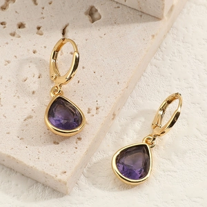 Detail of gold water drop earrings with purple gemstones on a natural stone surface