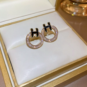 Macro detail of gold plated earring with black H letter and clear zircon round ring