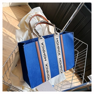 Detail of blue felt tote bag with beige MOMPICK handles and brown leather trim