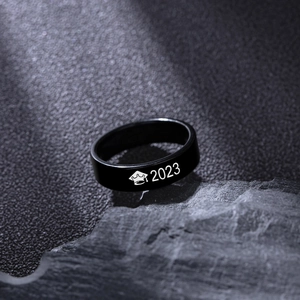 Black graduation 2023 ring with mortarboard cap icon on a textured stone surface