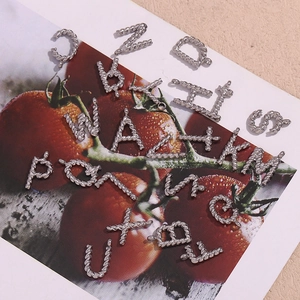 Detail of silver twisted texture alphabet pendants on a tomato pattern decorative card