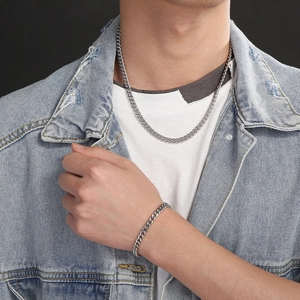 Detailed view of silver Cuban chain necklace and bracelet set on a denim-clad male model