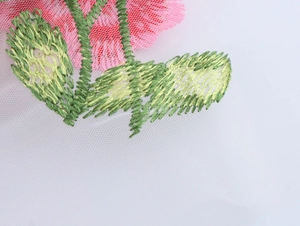 Gros plan détaillé des broderies de fleurs rouges et feuilles vertes sur tulle blanc