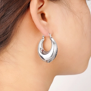 Macro detail of large polished silver teardrop hoop earrings worn by a model