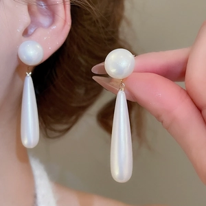 Detailed close-up showing large white pearl drop earrings worn on ear with golden metal finish